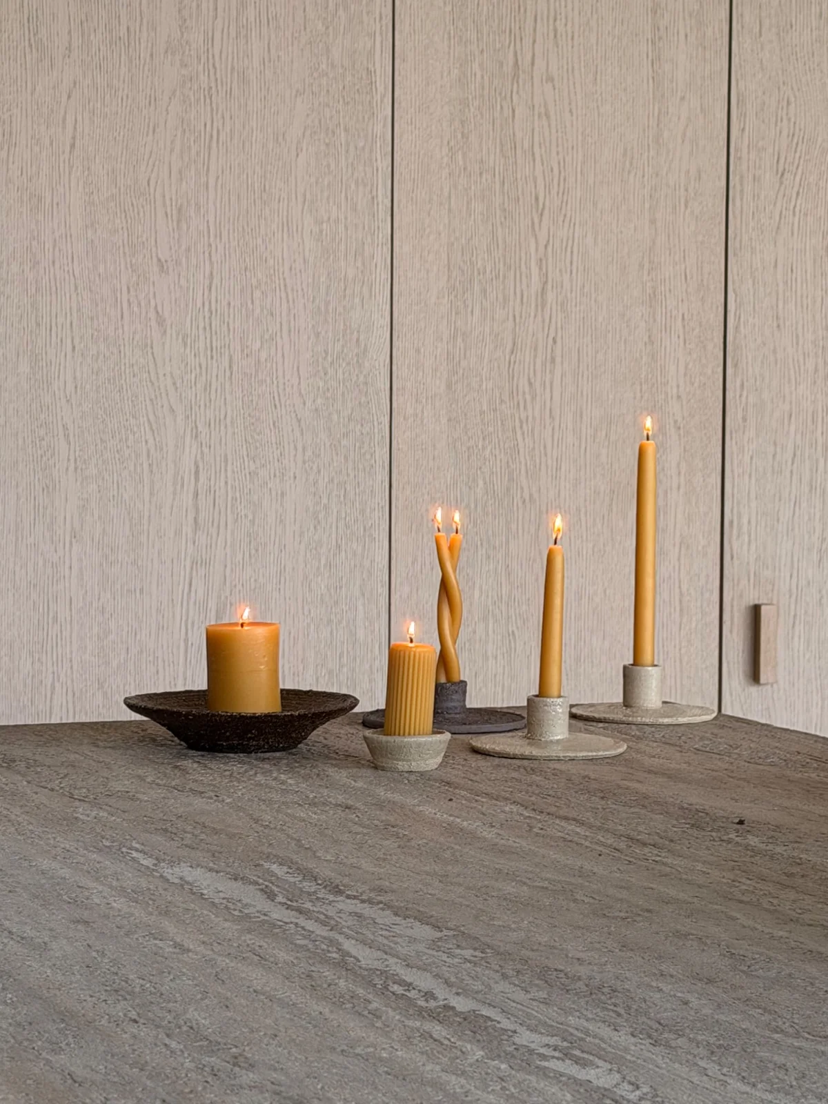 Brandende bijenwaskaarsen op keramieken houders, voor een licht houten kastenwand